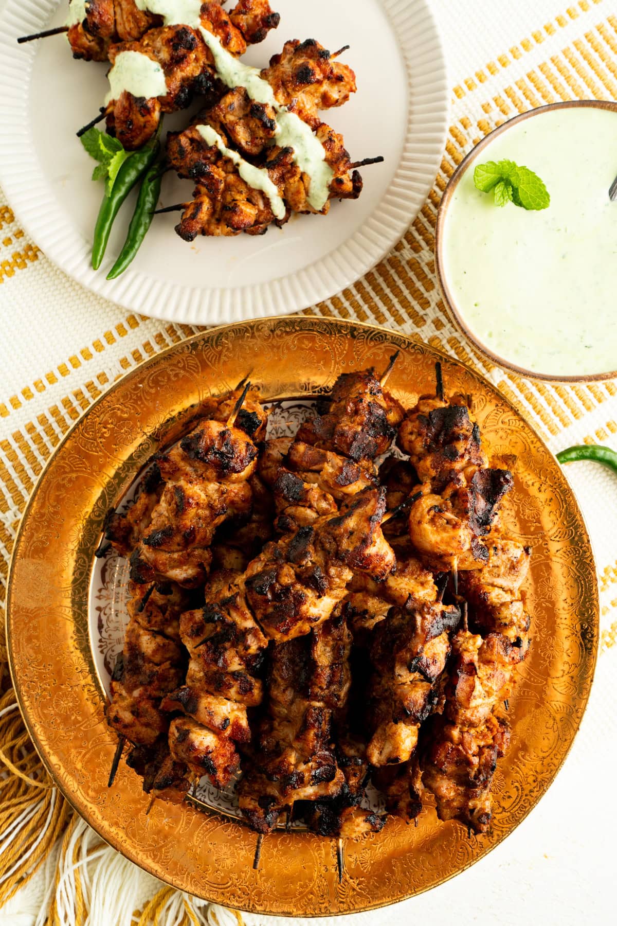 A gold rimmed plate of tandoori chicken skewers on a table.