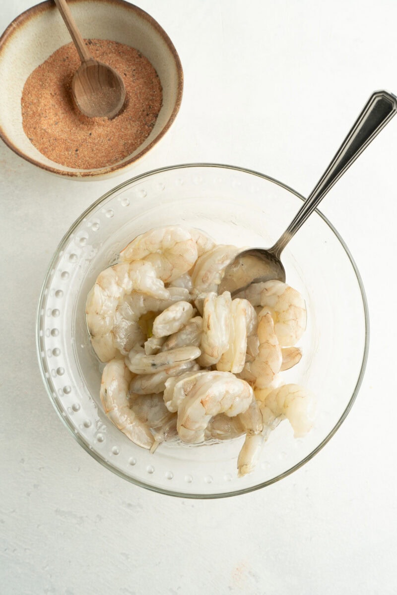 Shrimp being mixed in a bowl with olive oil.