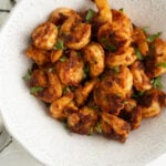 A bowl of pan seared shrimp on a blue and white striped tea towel.