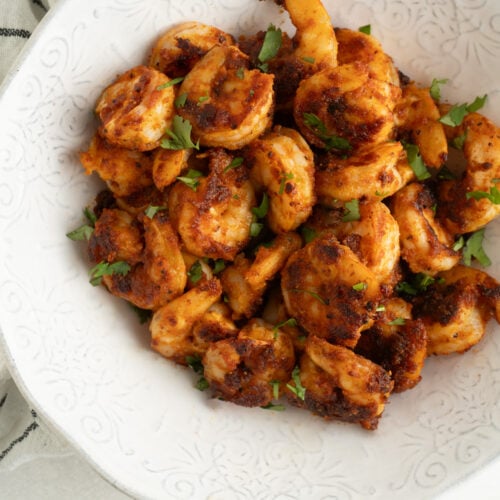 A bowl of pan seared shrimp on a blue and white striped tea towel.