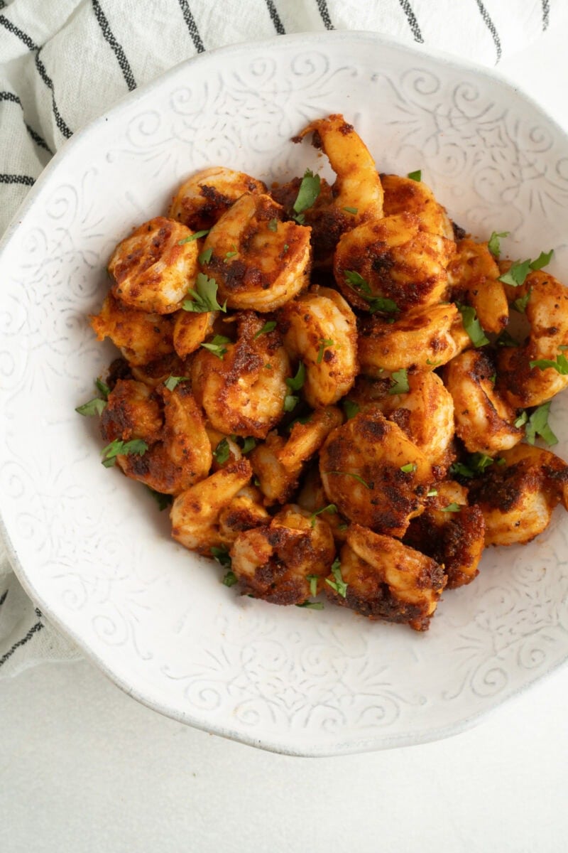 A bowl of pan seared shrimp on a blue and white striped tea towel.
