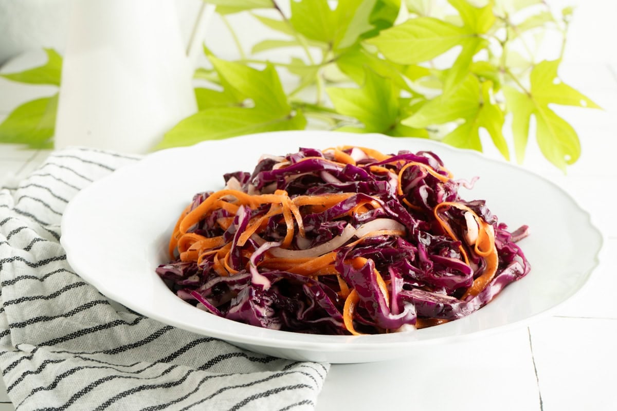 A bowl of purple cabbage cole slaw on a table with a striped napkin.