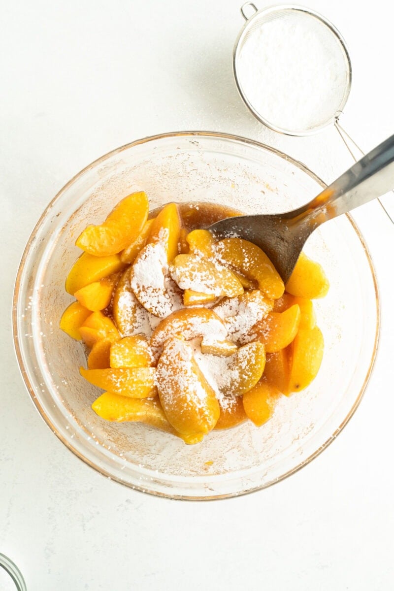 A bowl of peaches with some cornstarch sifted on top.