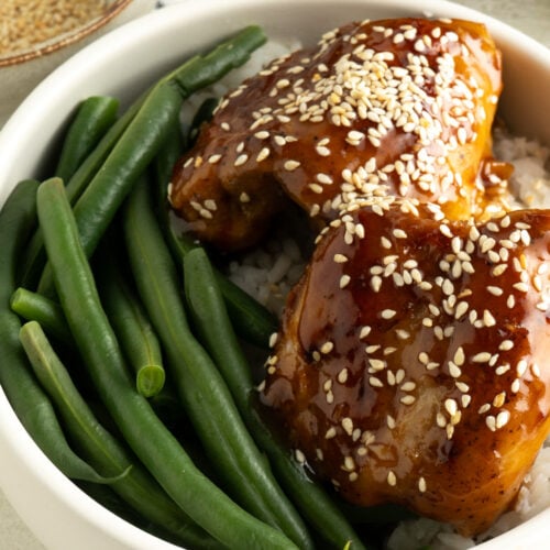 A bowl of teriyaki glazed chicken thighs with rice and green beens.