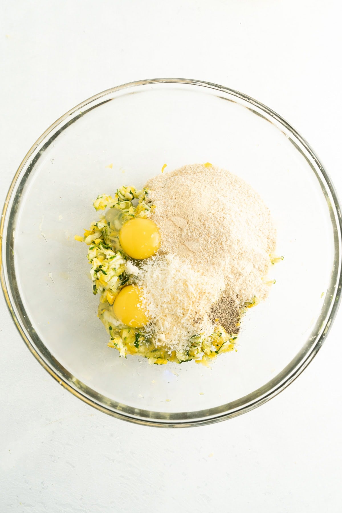 A bowl of shredded zucchini, eggs, bread crumbs and parmesan.
