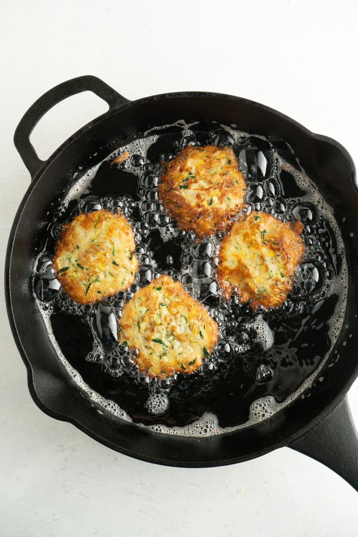 Zucchini fritters frying in a pan.