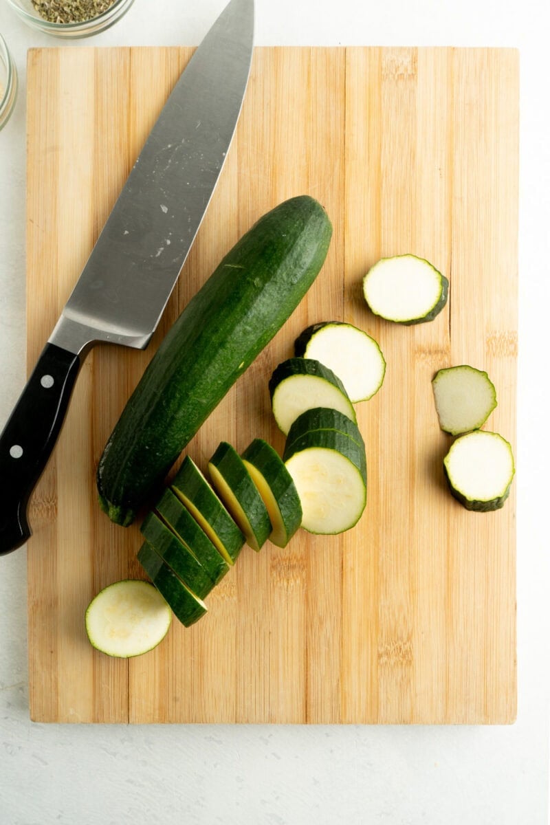 Zucchini being sliced on a cutting board.