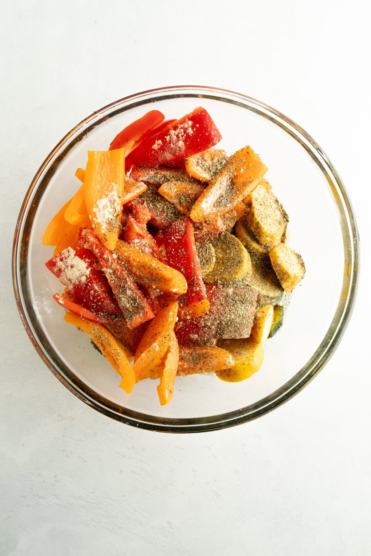 A bowl of peppers and zucchini with olive oil and seasonings.