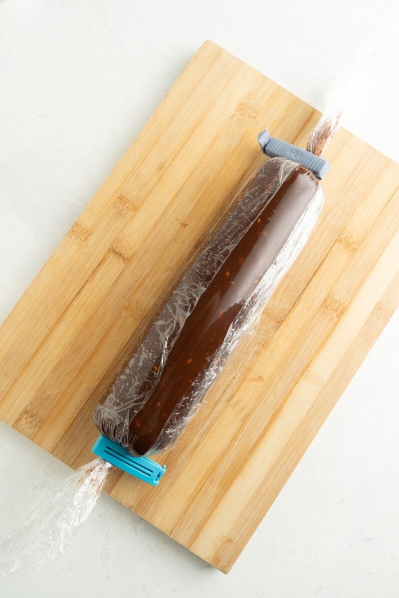 A roll of chocolate salami covered in plastic wrap and sealed on the ends.