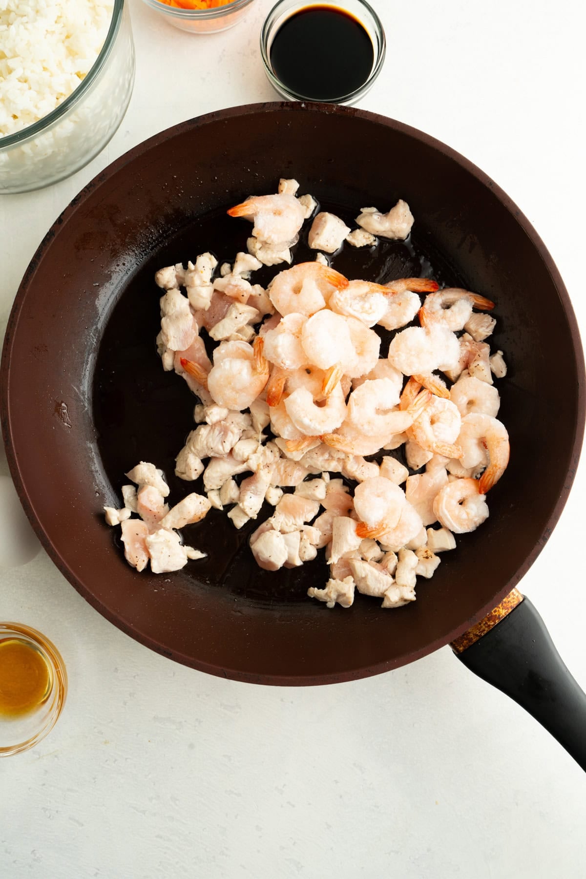 A pan of chicken pieces and frozen shrimp being cooked.