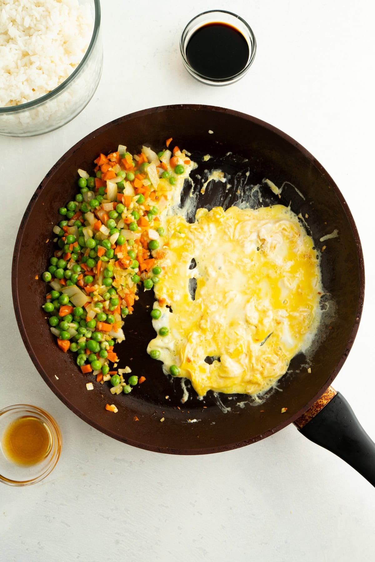 Vegetables on one side of a large pan and an egg being scrambled on the other side.