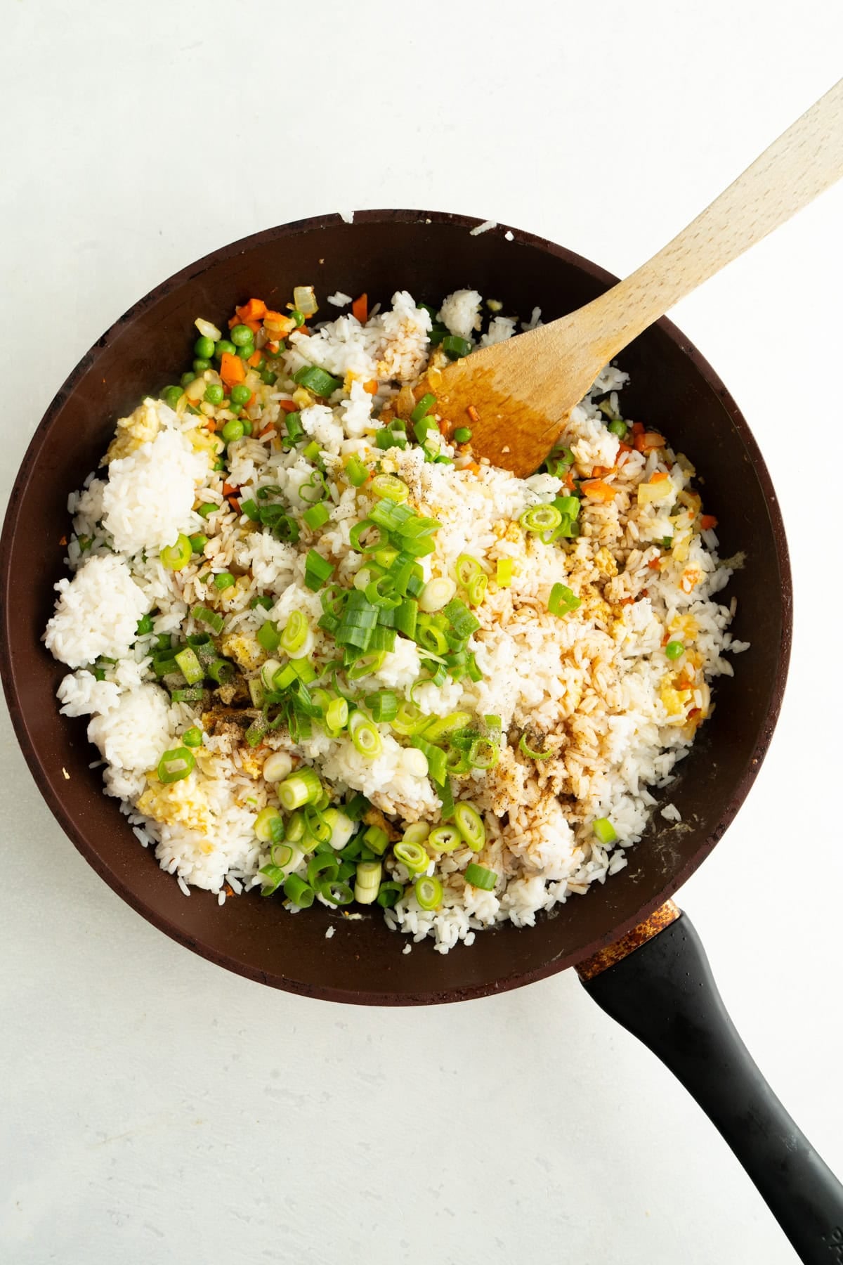 A large pan filled with vegetables and white rice being mixed with soy sauce.
