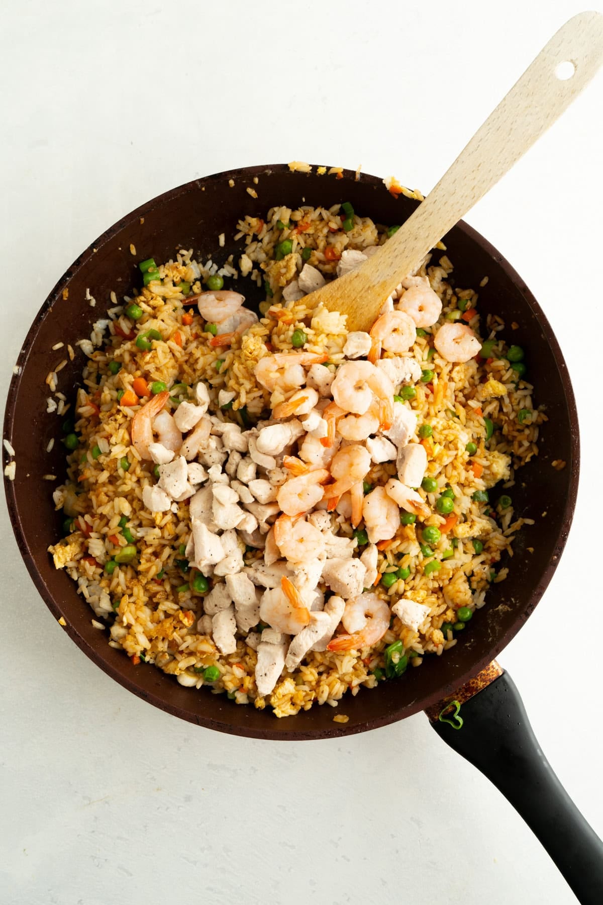 Cooked chicken and shrimp being added a pan of vegetable fried rice.