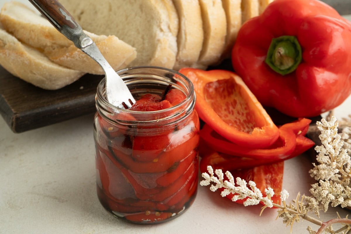 Roasted peppers on a table with a fork inside the jar.