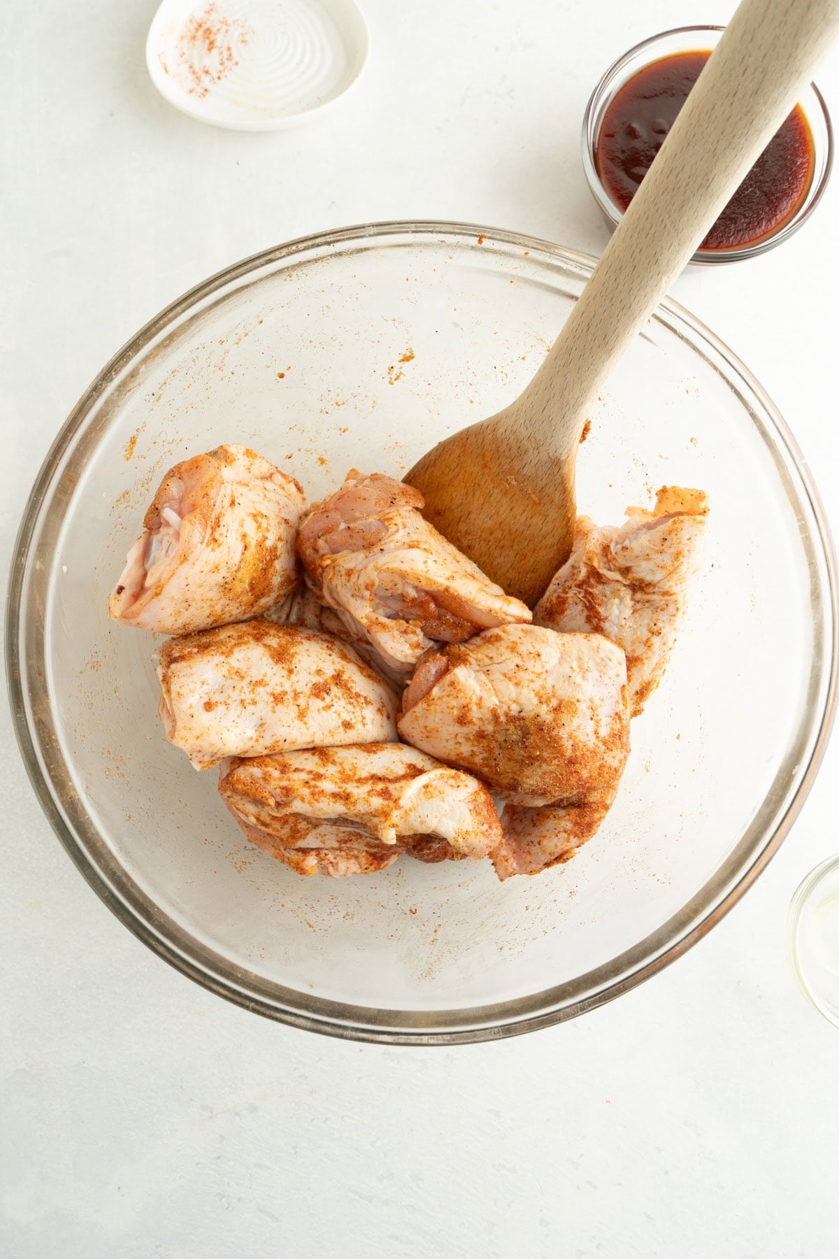 A bowl of chicken thighs being mixed with seasonings.