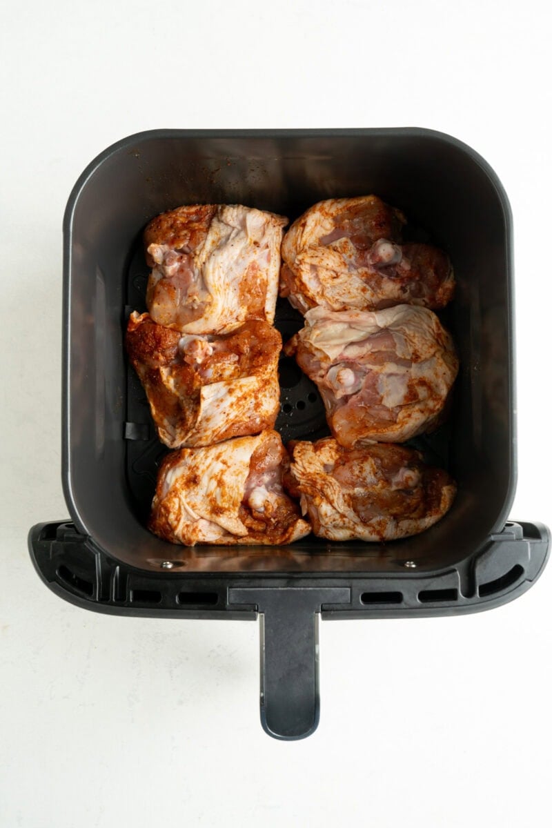 Chicken thighs skin side down in an air fryer basket.