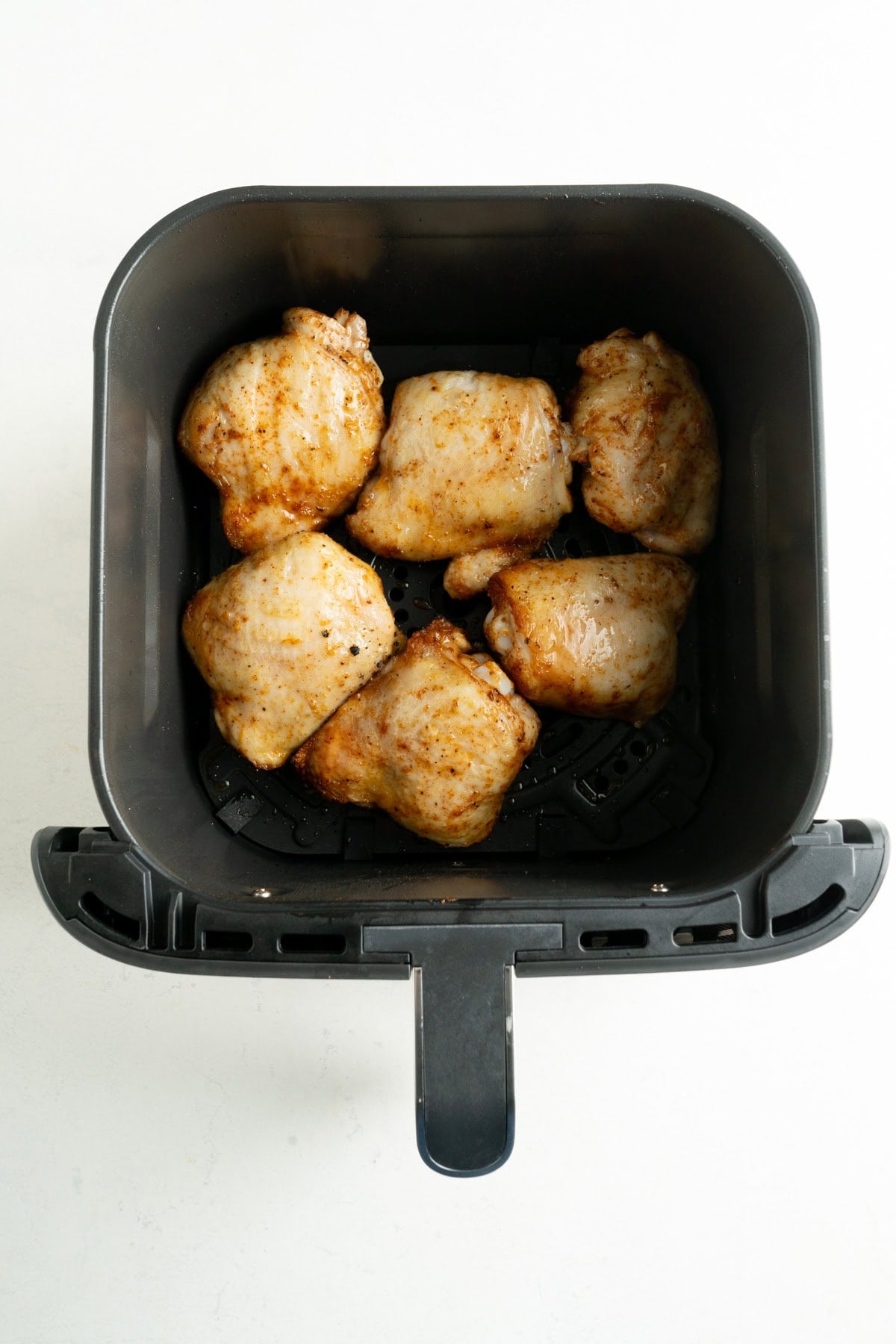Chicken thighs skin-side up in an air-fryer basket.