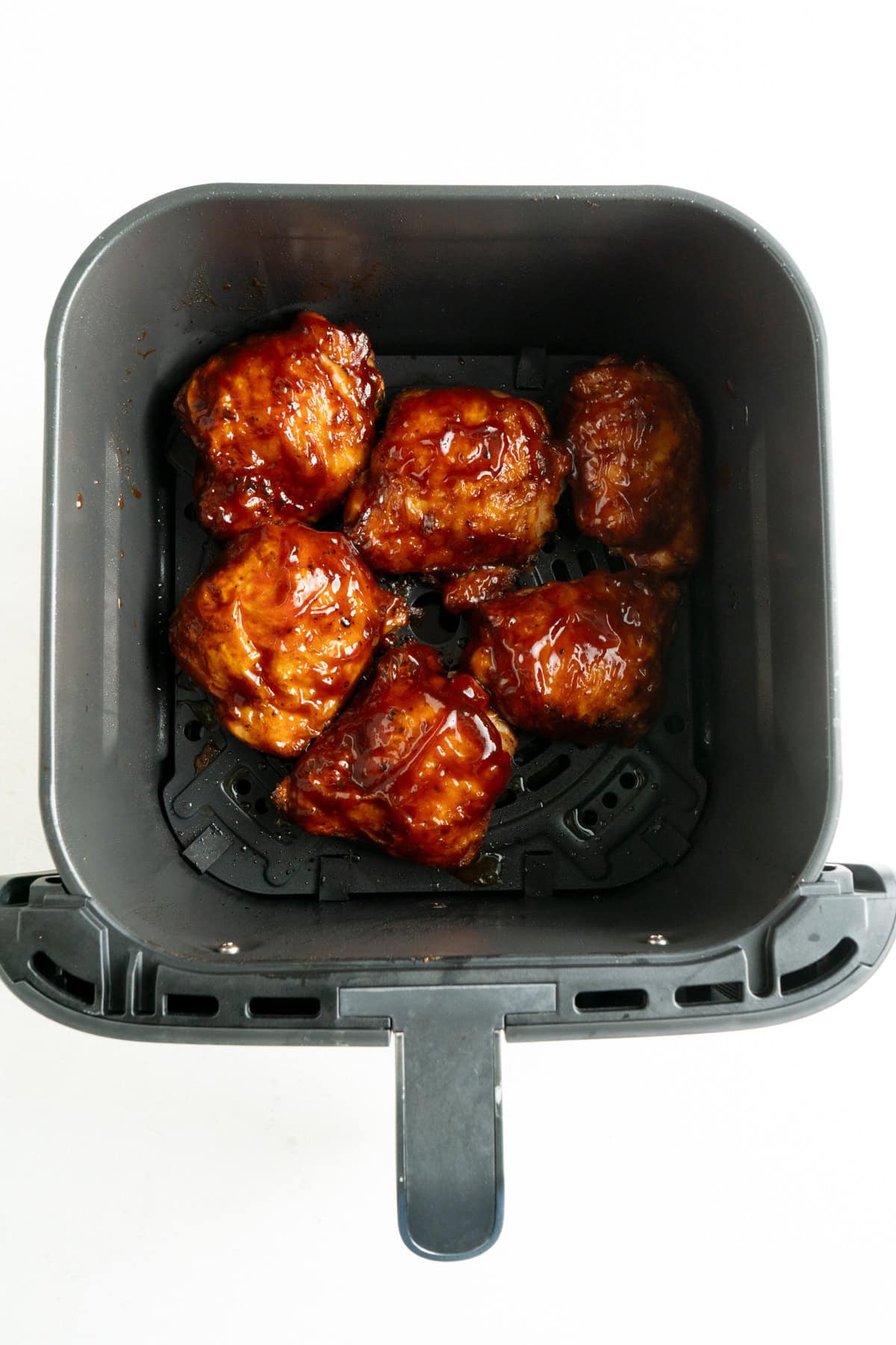 Chicken thighs basted with BBQ sauce in an air fryer basket.