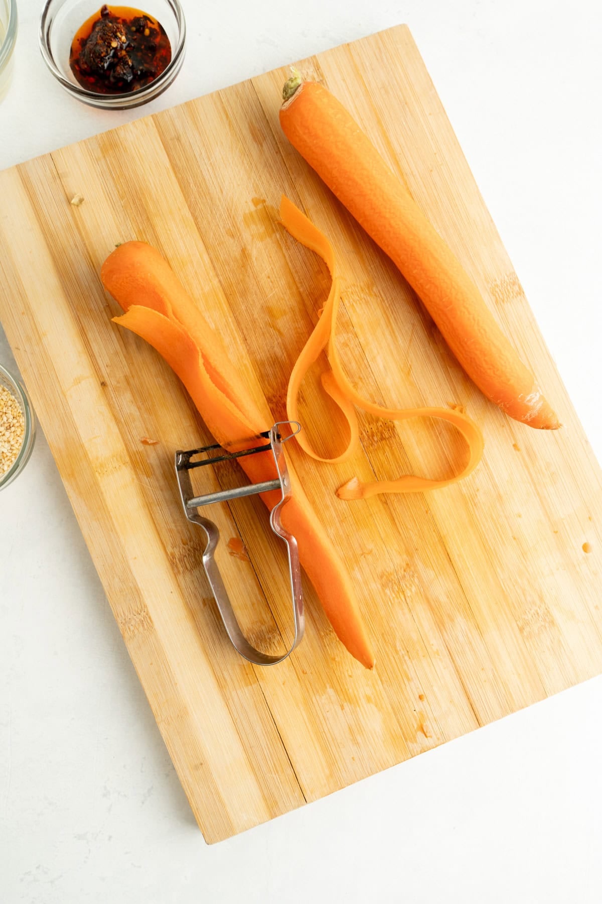 Carrots being shaved with a peeler into ribbons on a cutting board.
