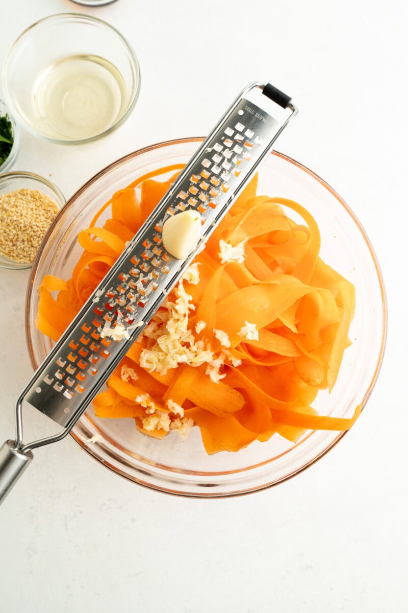 Sweet potato garlic mash ingredients with garlic grater, bowls of seasoning and water, on white background.