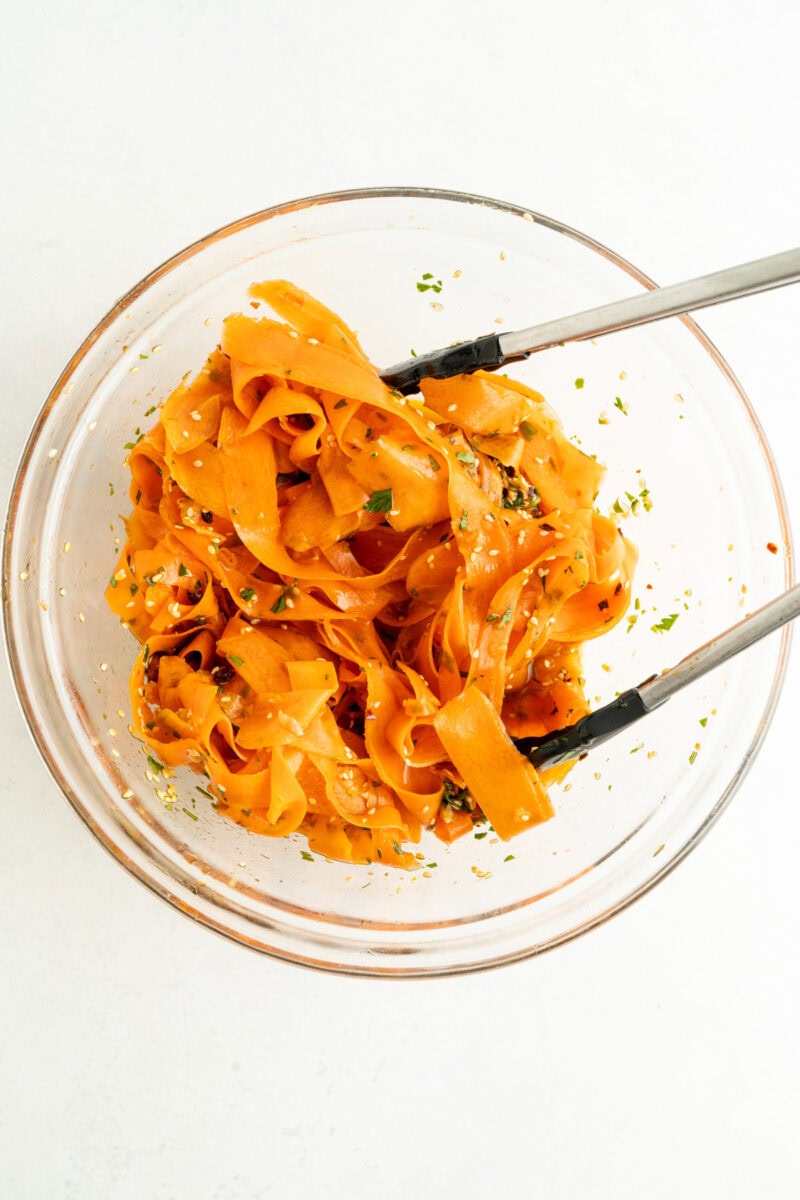 A raw carrot salad being tossed with a spicy Asian dressing.