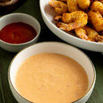 A bowl of bang bang sauce near a plate of breaded shrimp.