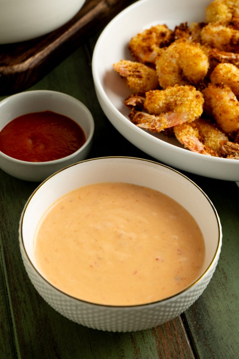A bowl of bang bang sauce near a plate of breaded shrimp.