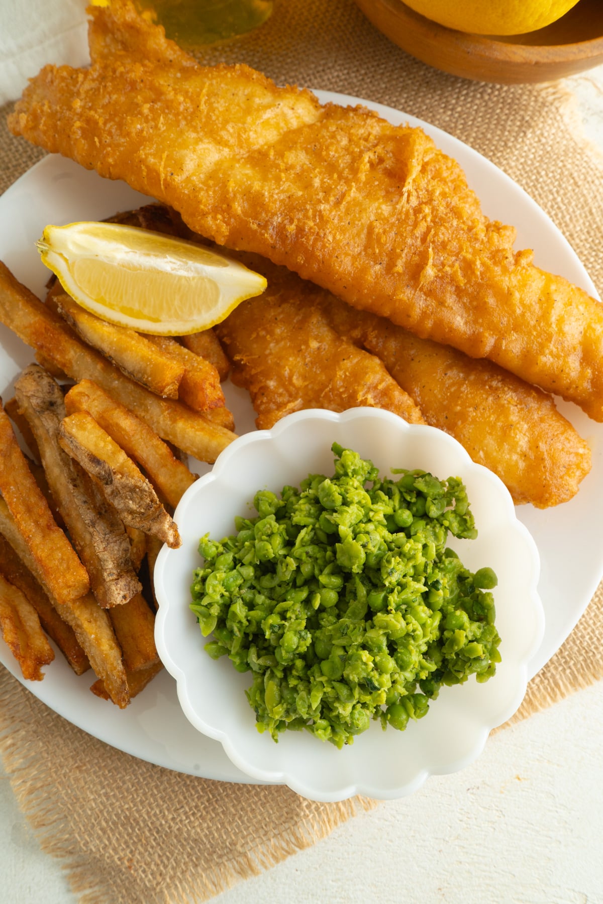 A  bowl of mushy peas o a plate of fish and chips.