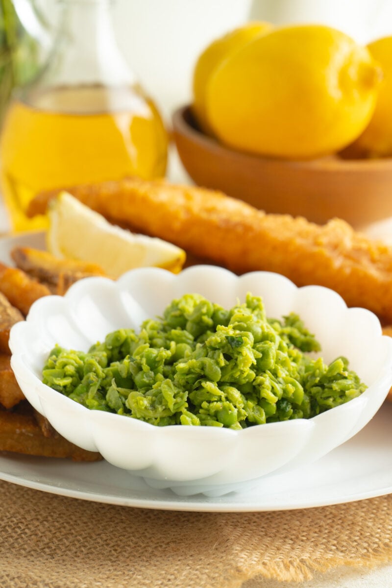 A bowl of mushy peas served on a table with fish and chips.