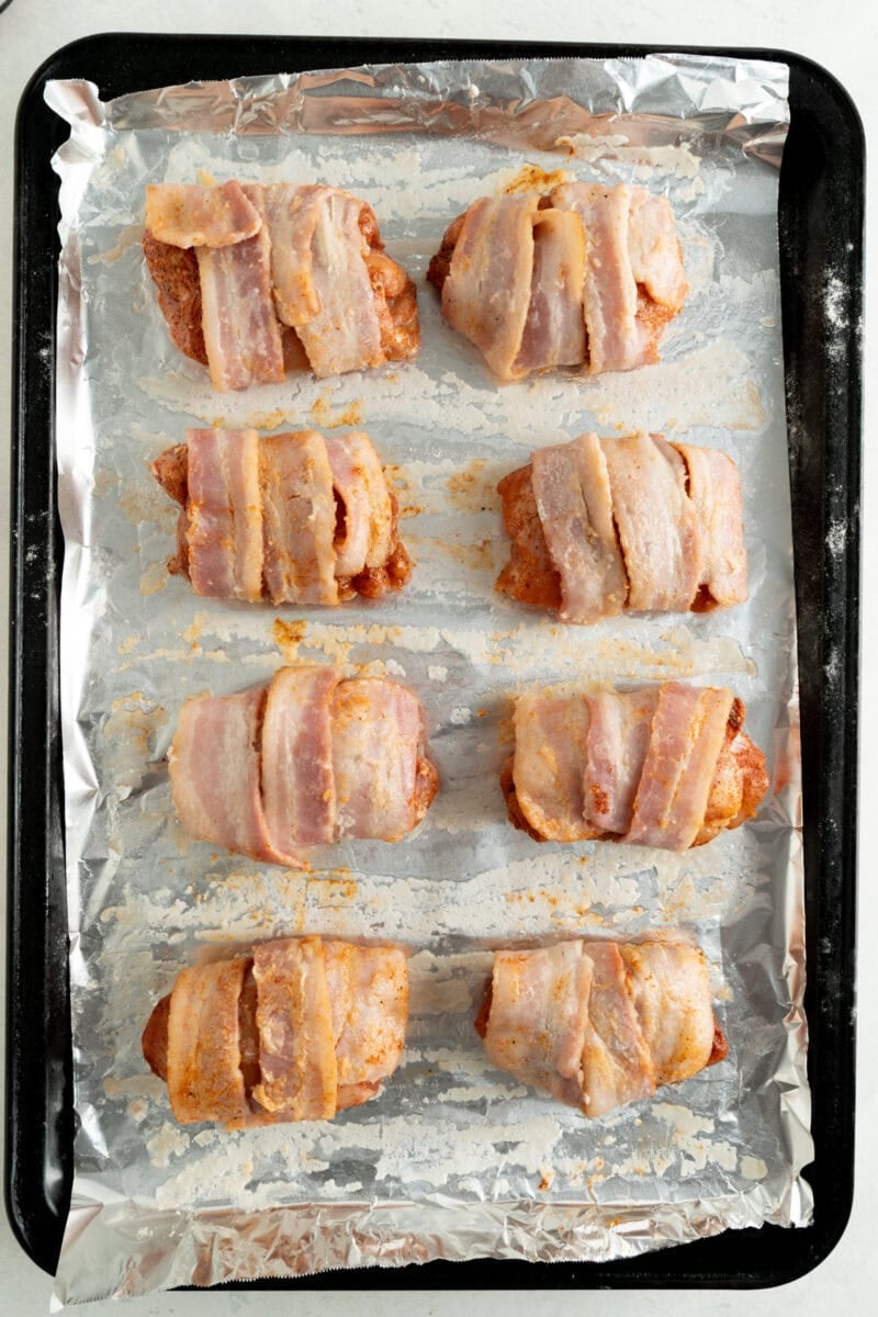 Uncooked bacon wrapped around seasoned chicken thighs and place on a foil lined baking sheet.