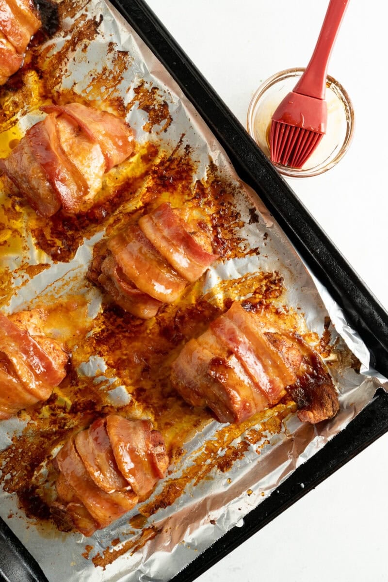 Baked bacon wrapped chicken thighs being based with hot honey.