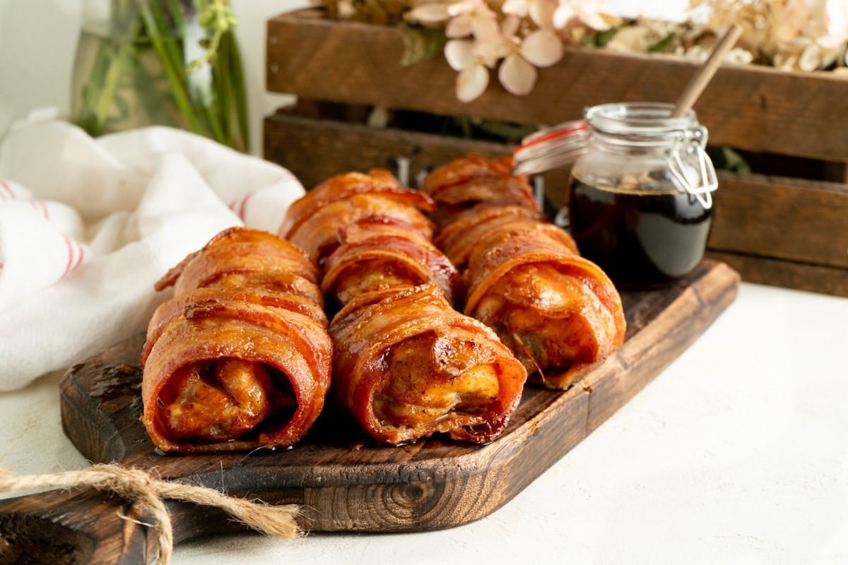 A platter or bacon wrapped oven baked chicken thighs on a wood platter on a table.