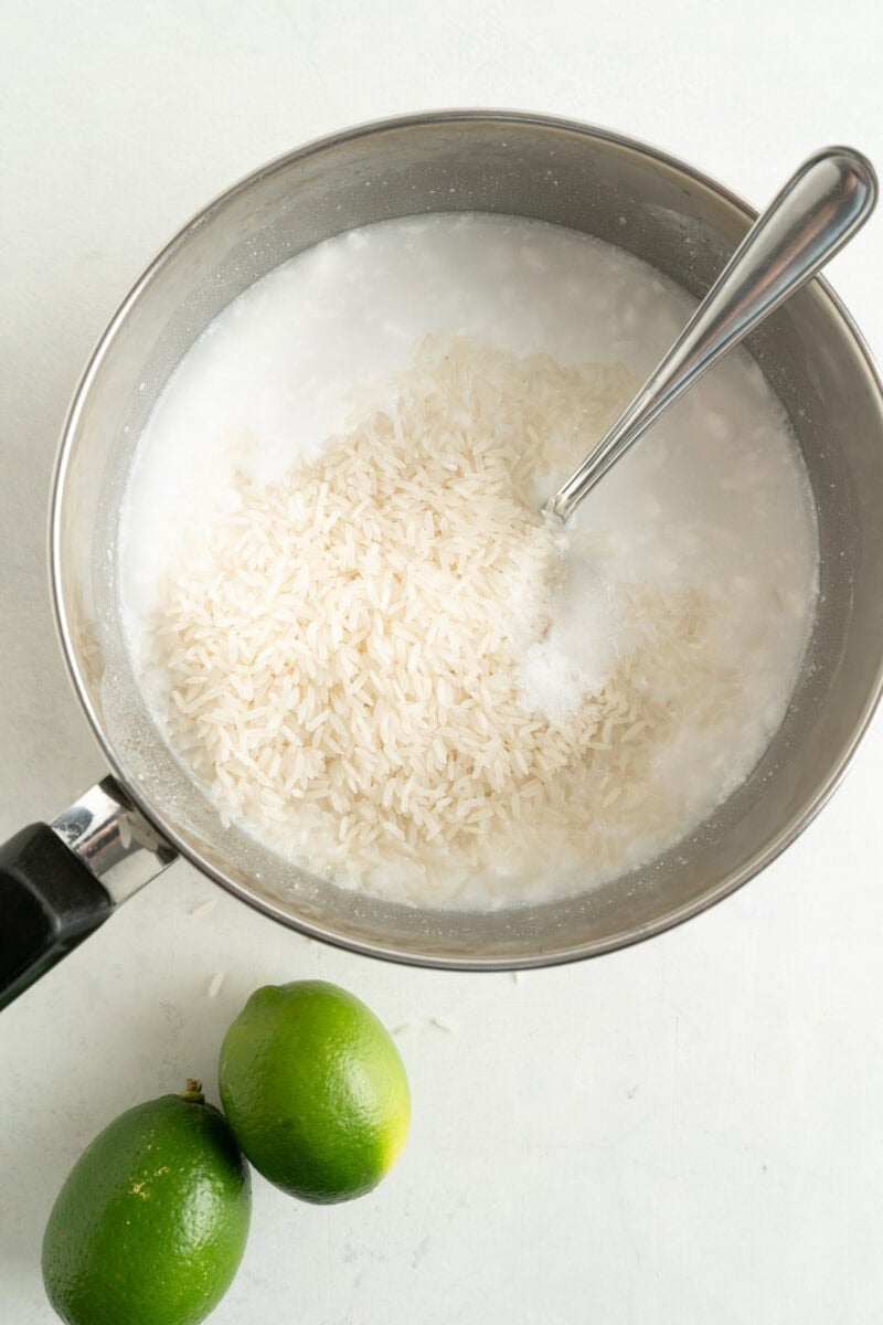 A pot of coconut and uncooked rice being added.