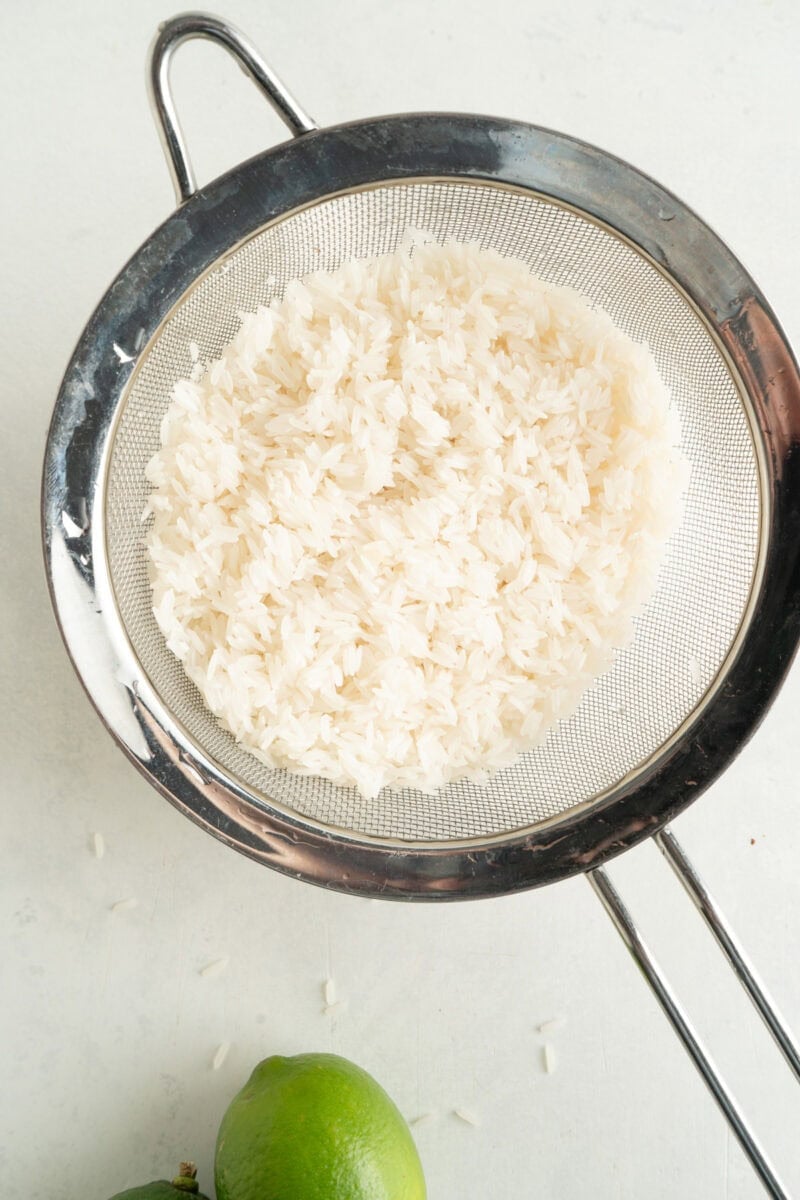 Rinsed rice in a fine meshed seive.