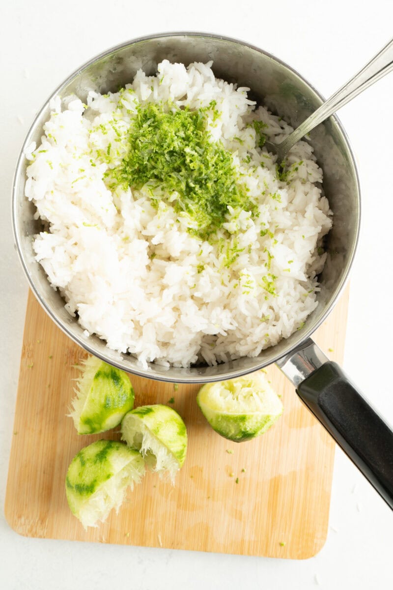 Fluffy cooked rice in a pot with lime zest and juice being mixed in.