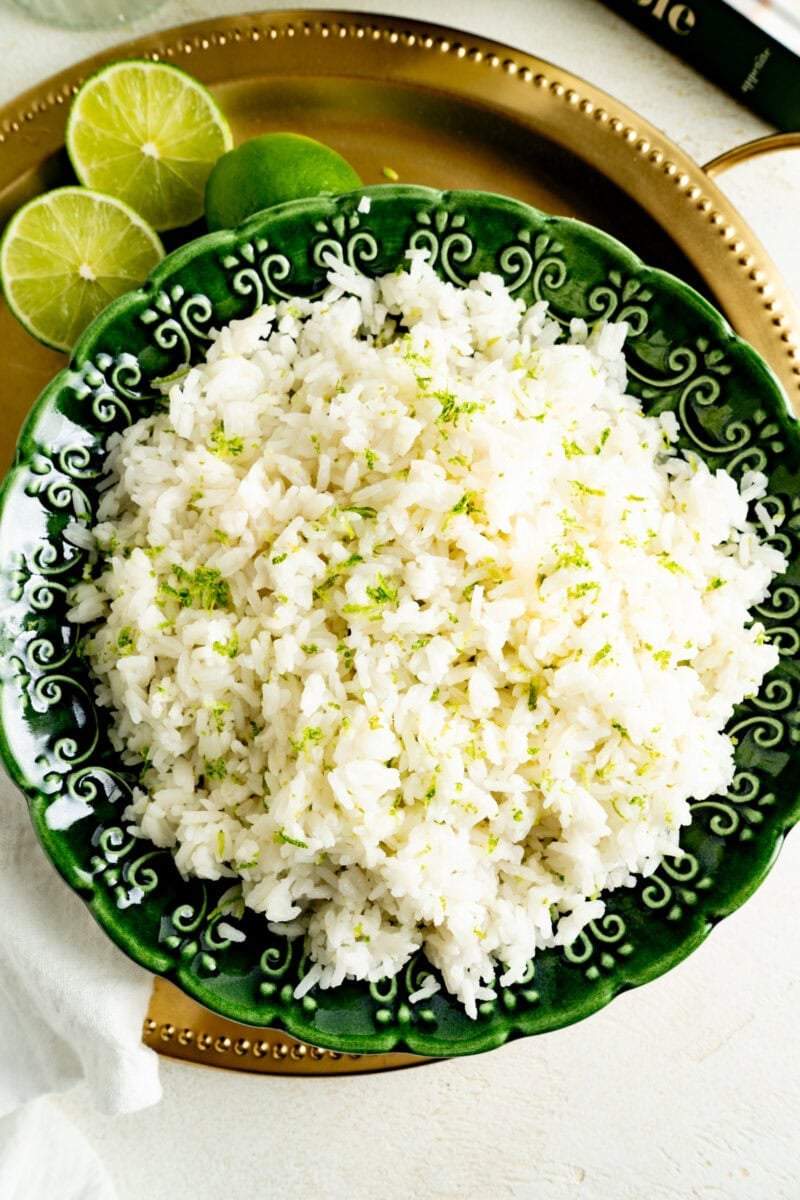 Pic of a bowl of coconut rice from overhead on a gold serving tray with limes.