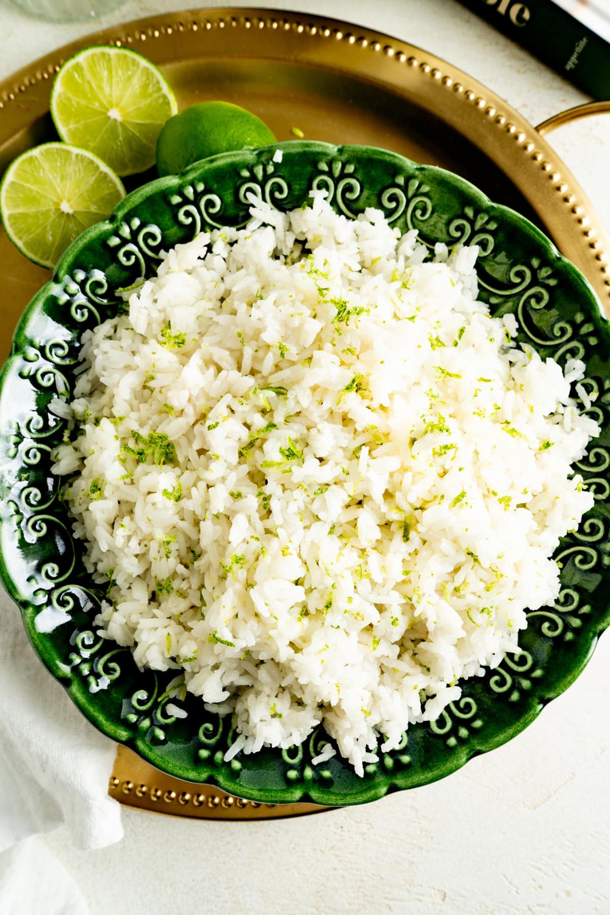 Pic of a bowl of coconut rice from overhead on a gold serving tray with limes.