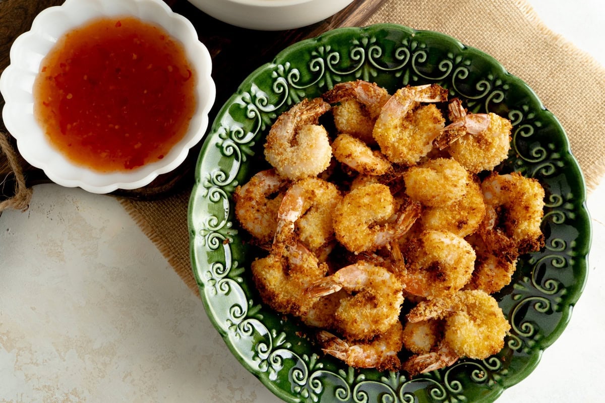 A bowl of panko fried shrimp on a table with sweet chili sauce.