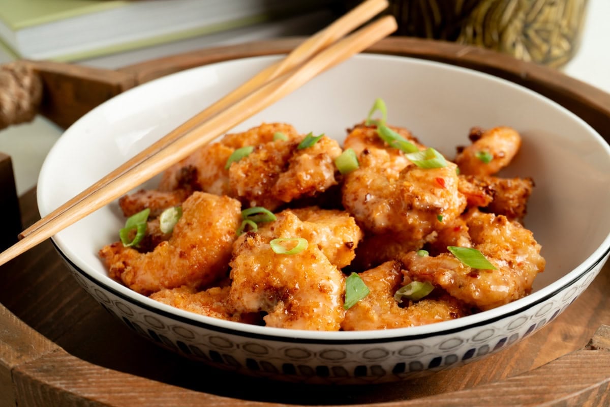 A bowl of bang bang shrimp on a table without chopsticks.