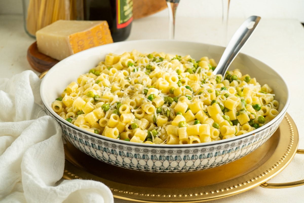 A bowl of pasta e piselli on a table with a serving spoon.