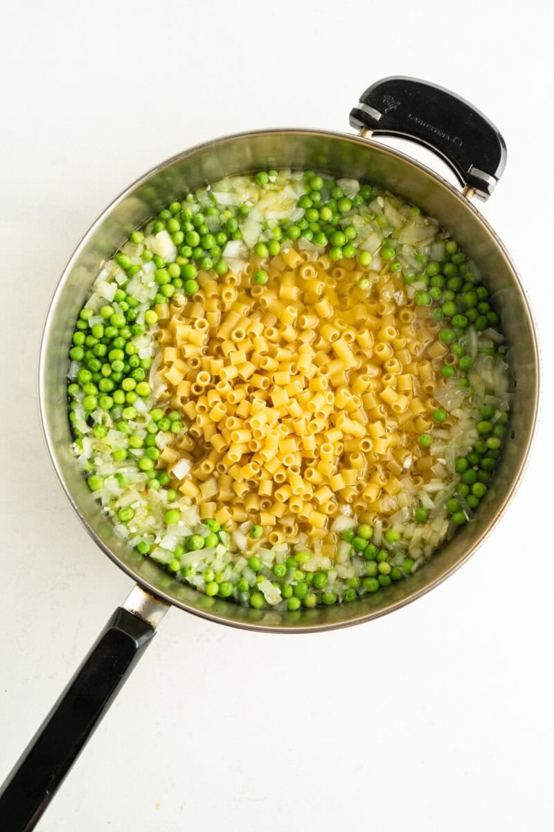 A deep sided pan filled with raw pasta e piselli ingredients.
