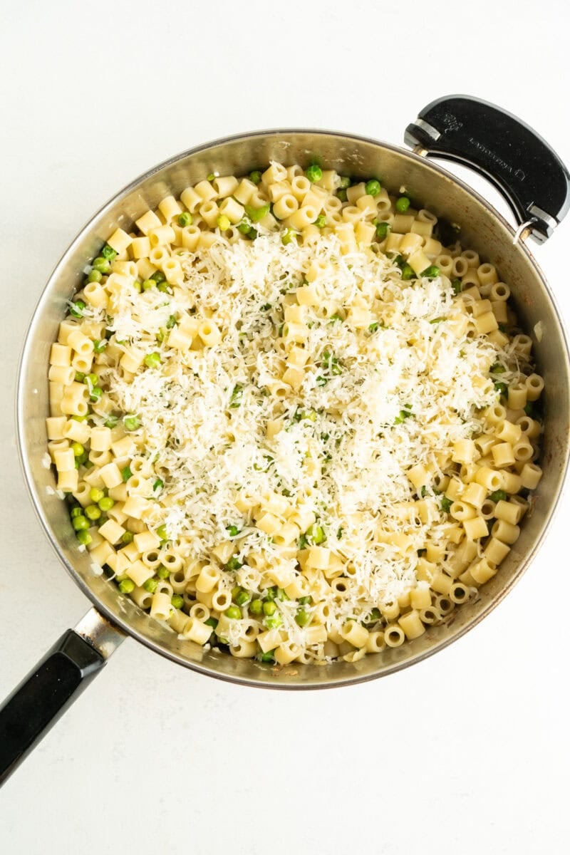 A pot of peas and pasta with shredded cheese on top.
