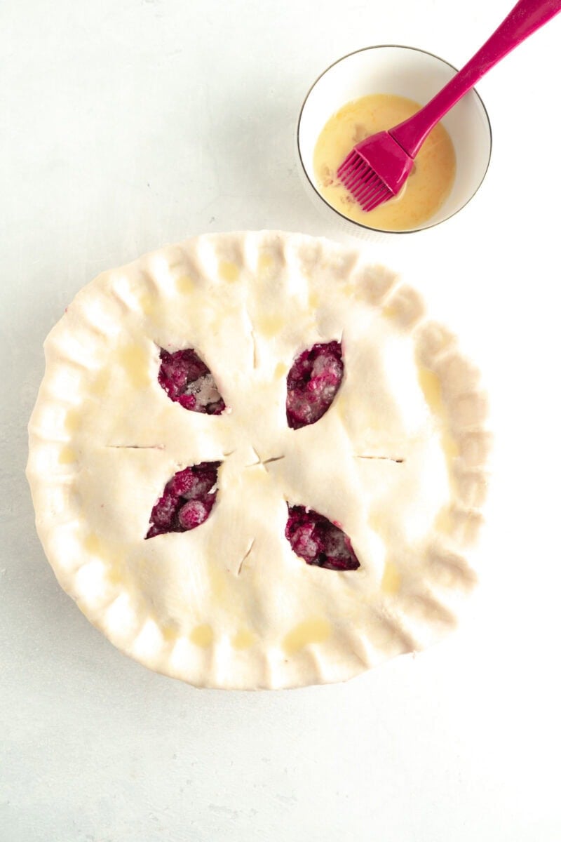 An unbaked pie being basted with egg wash.