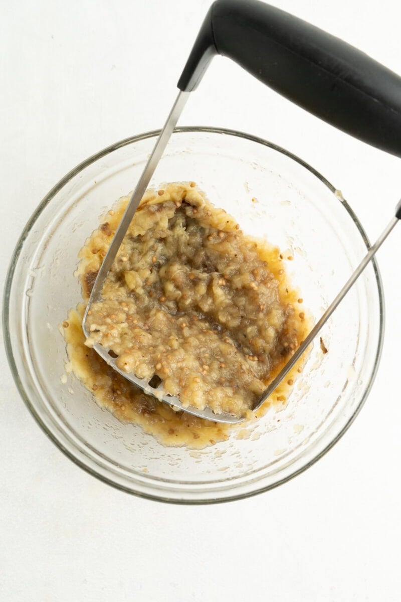 Cooked eggplant being mashed in a bowl.