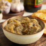 A bowl of eggplant spread on a table and wooden board.