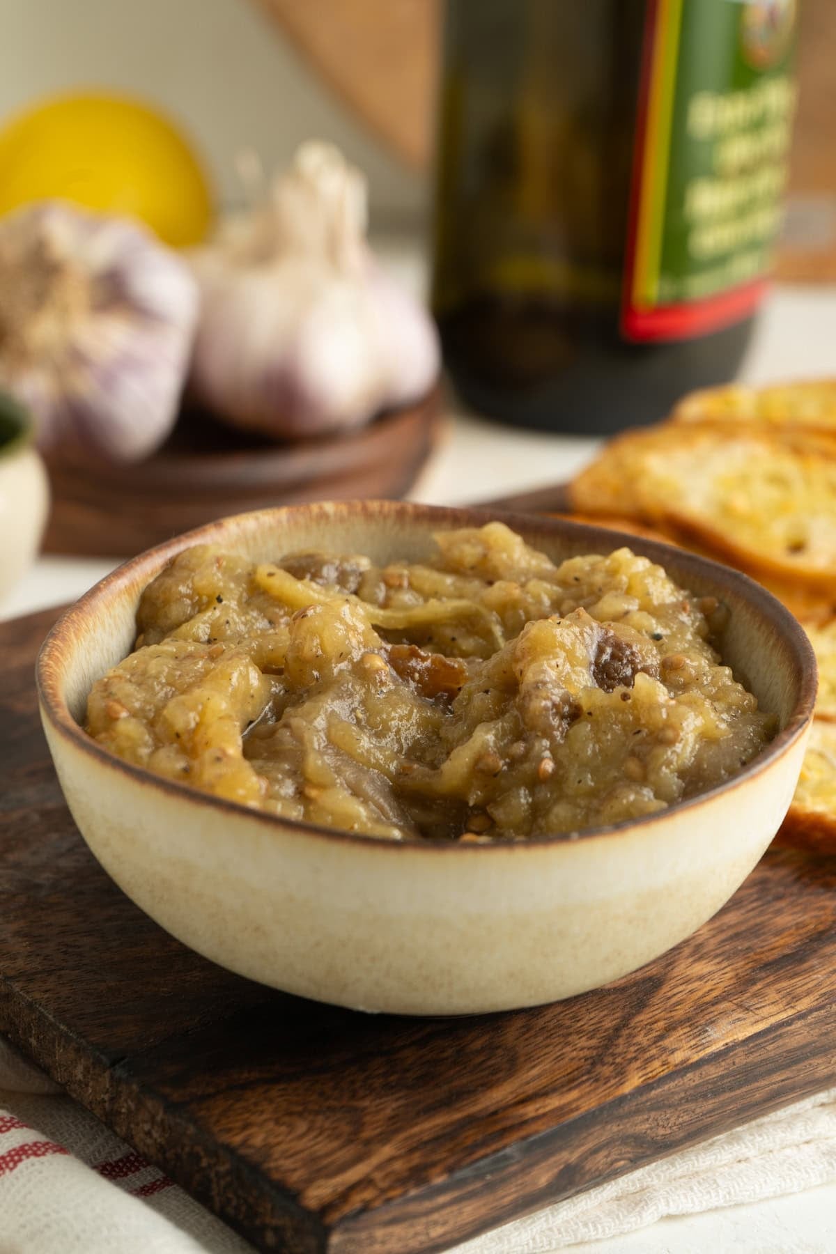 A bowl of eggplant spread on a table and wooden board.