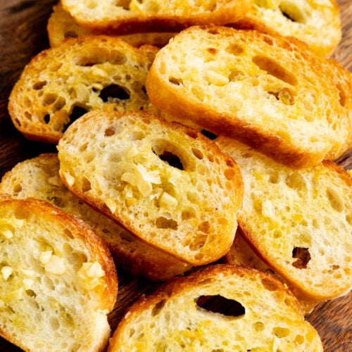A pile of crostini crackers on a cutting board.