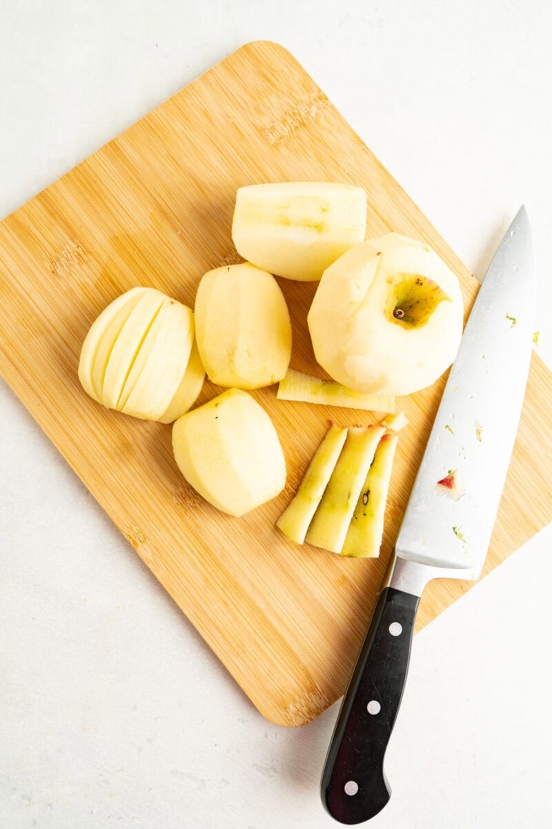 Peeled apples being sliced on a cutting board.