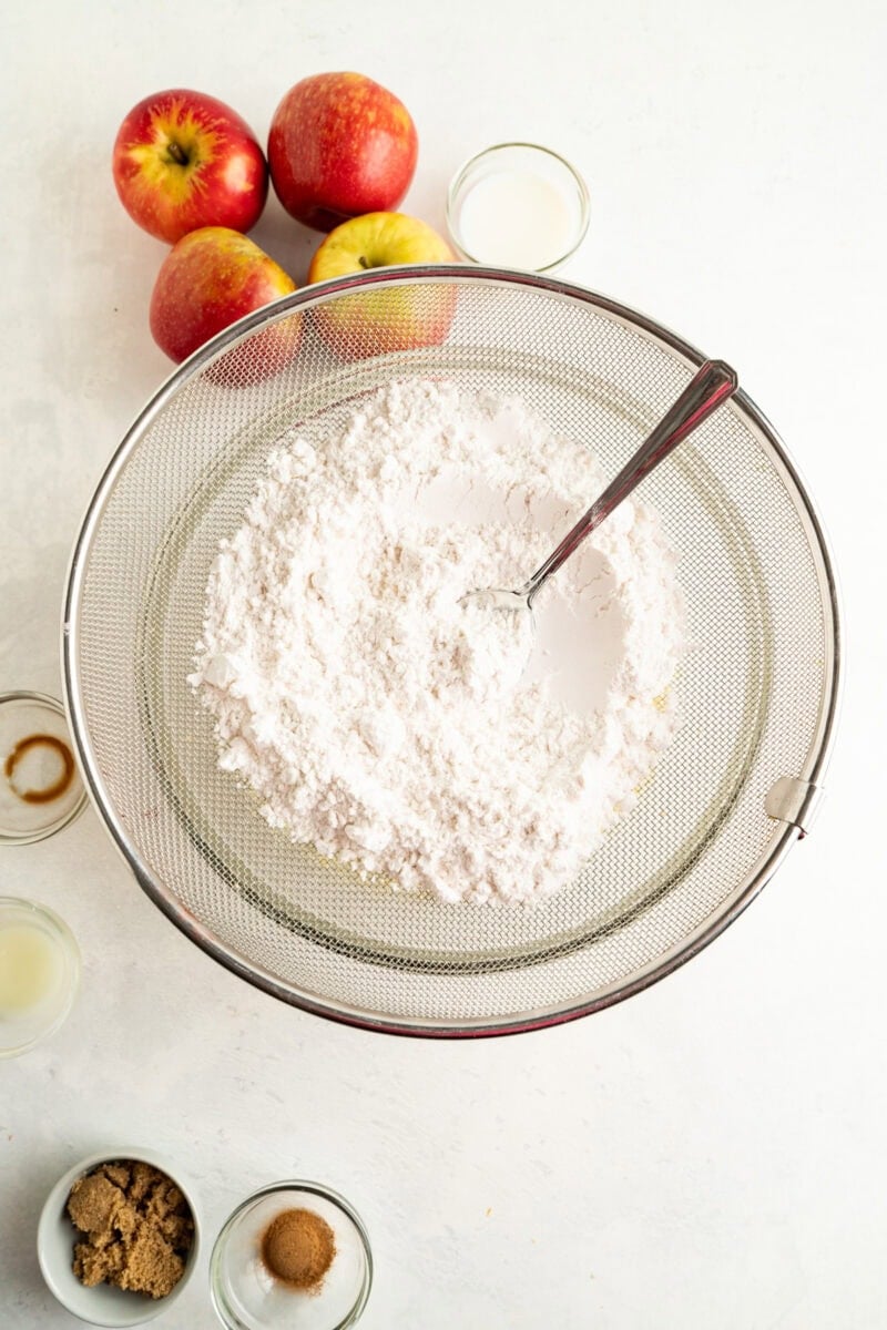 A sieve of flour and a spoon over a bowl.