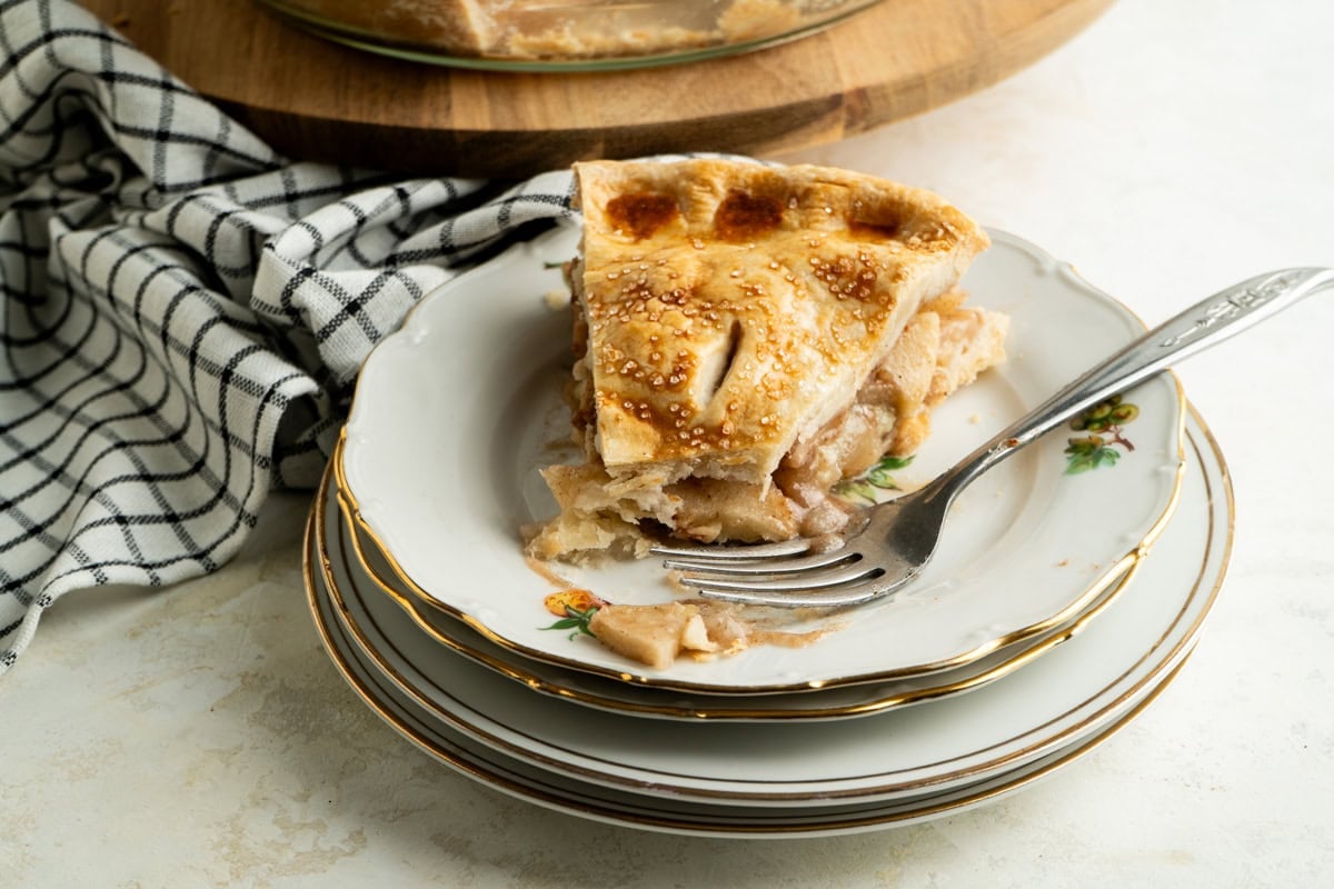 A slice of apple pie with a fork after a bite has been taken.